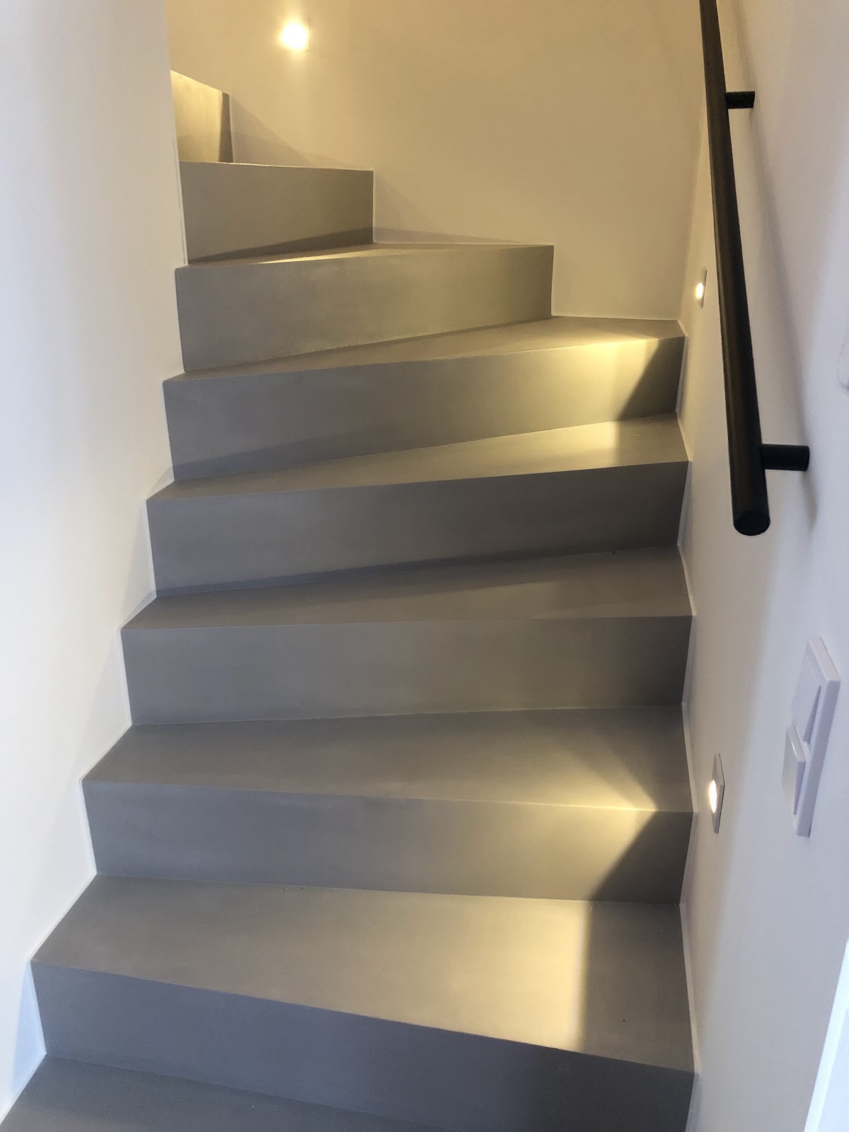 Modern gestaltete, gewendelte Treppe in grauer Betonoptik mit indirekter Stufenbeleuchtung.