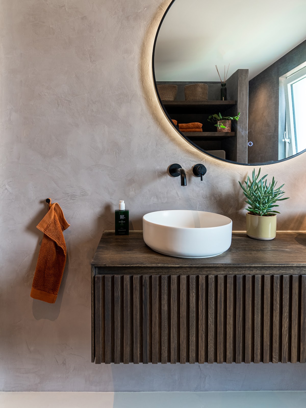 Modernes Badezimmer mit fugenloser grauer Spachtelwand und rundem Spiegel über einem Waschplatz.