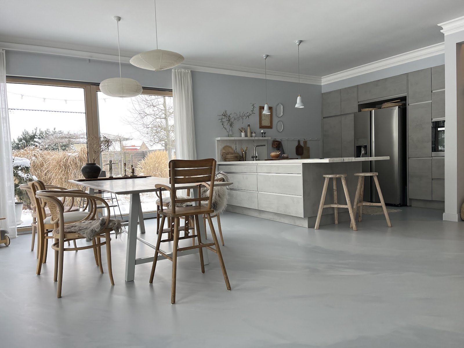 Offene moderne Küche mit fugenlosem hellgrauen Boden in Betonoptik und einem Essbereich mit Holzhockern.
