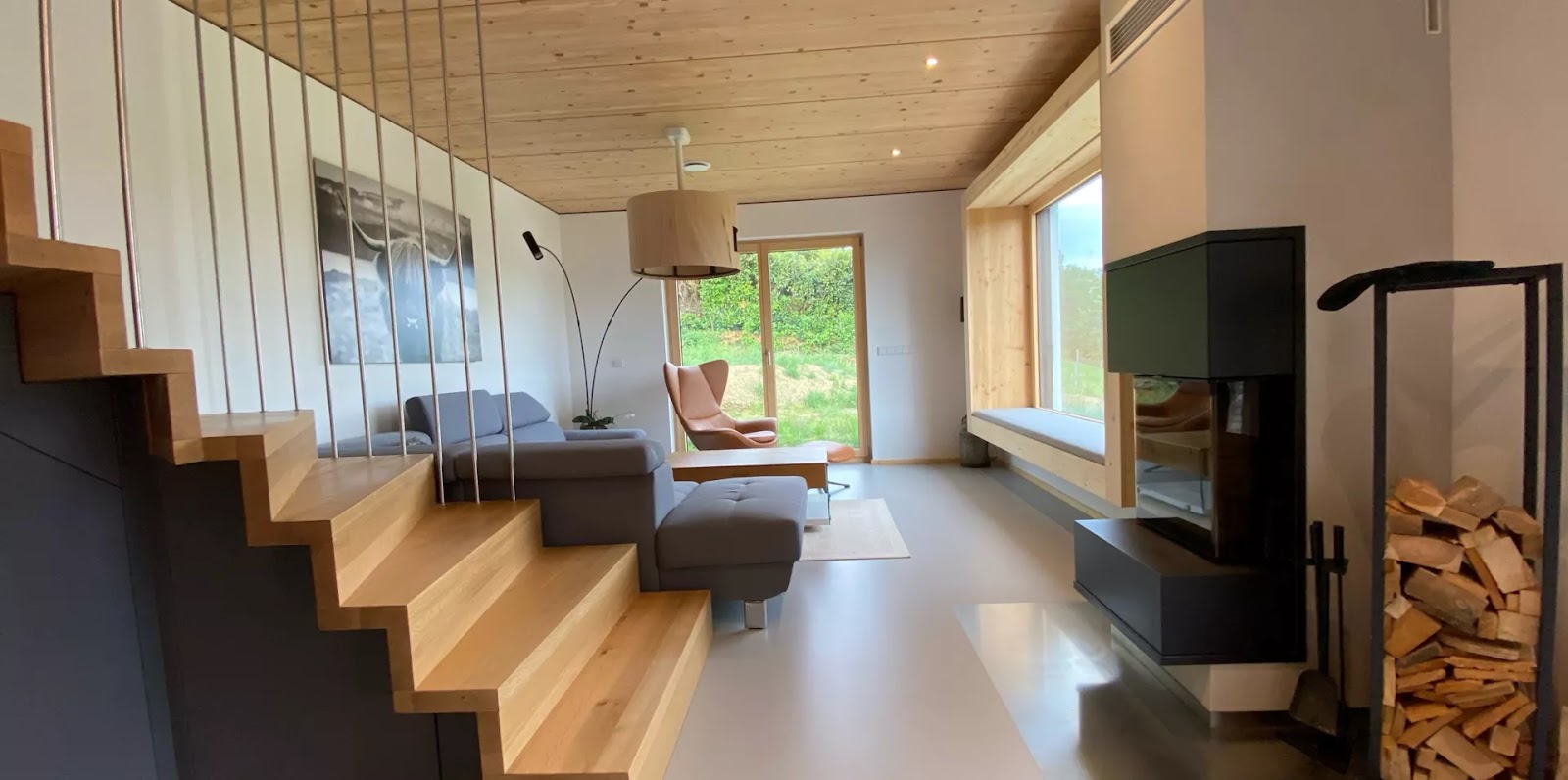 Moderner Wohnraum mit hellem, fugenlosem Bodenbelag und Holztreppe bei Tageslicht.