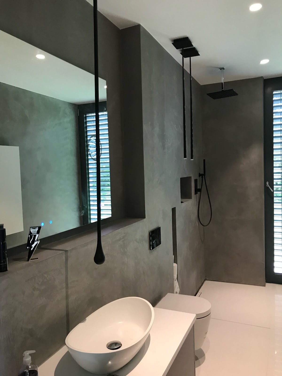 Modernes Badezimmer mit Wänden in grauer Betonoptik und einem weißen Aufsatzwaschbecken.