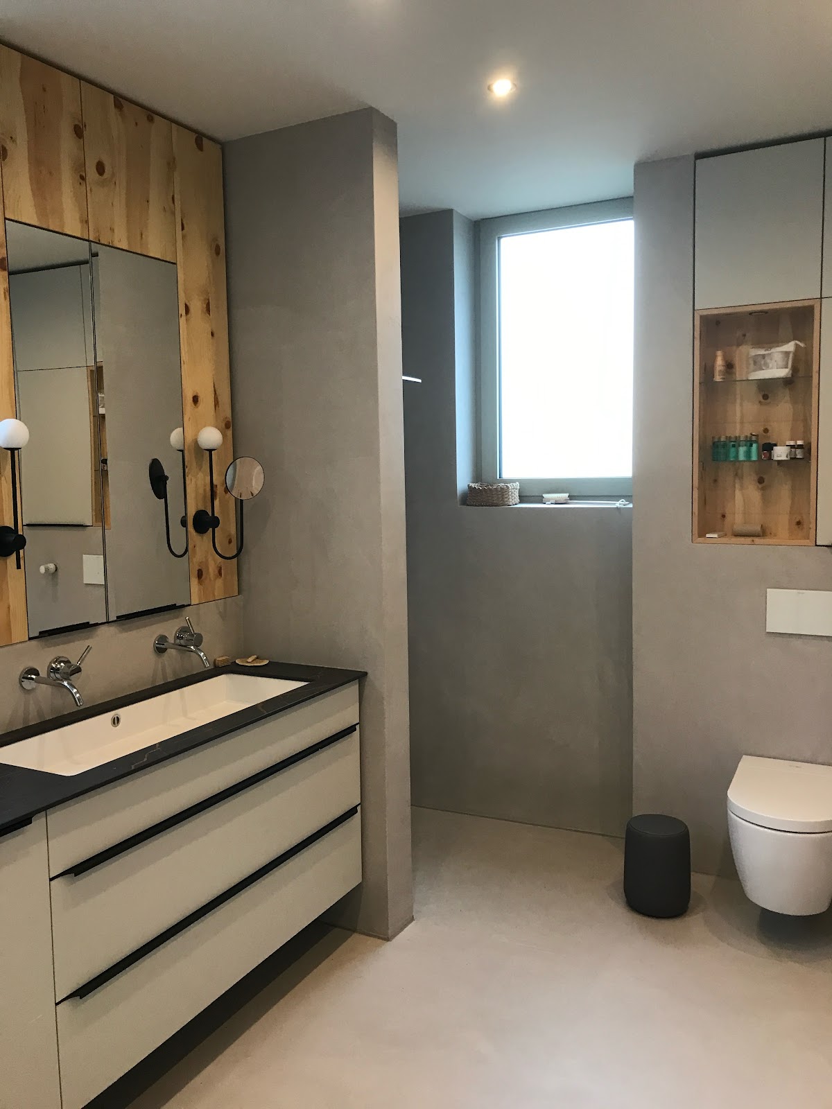 Modernes Badezimmer mit fugenlosen Wänden in grauer Betonoptik und einem Waschtisch mit Echtholzakzenten.
