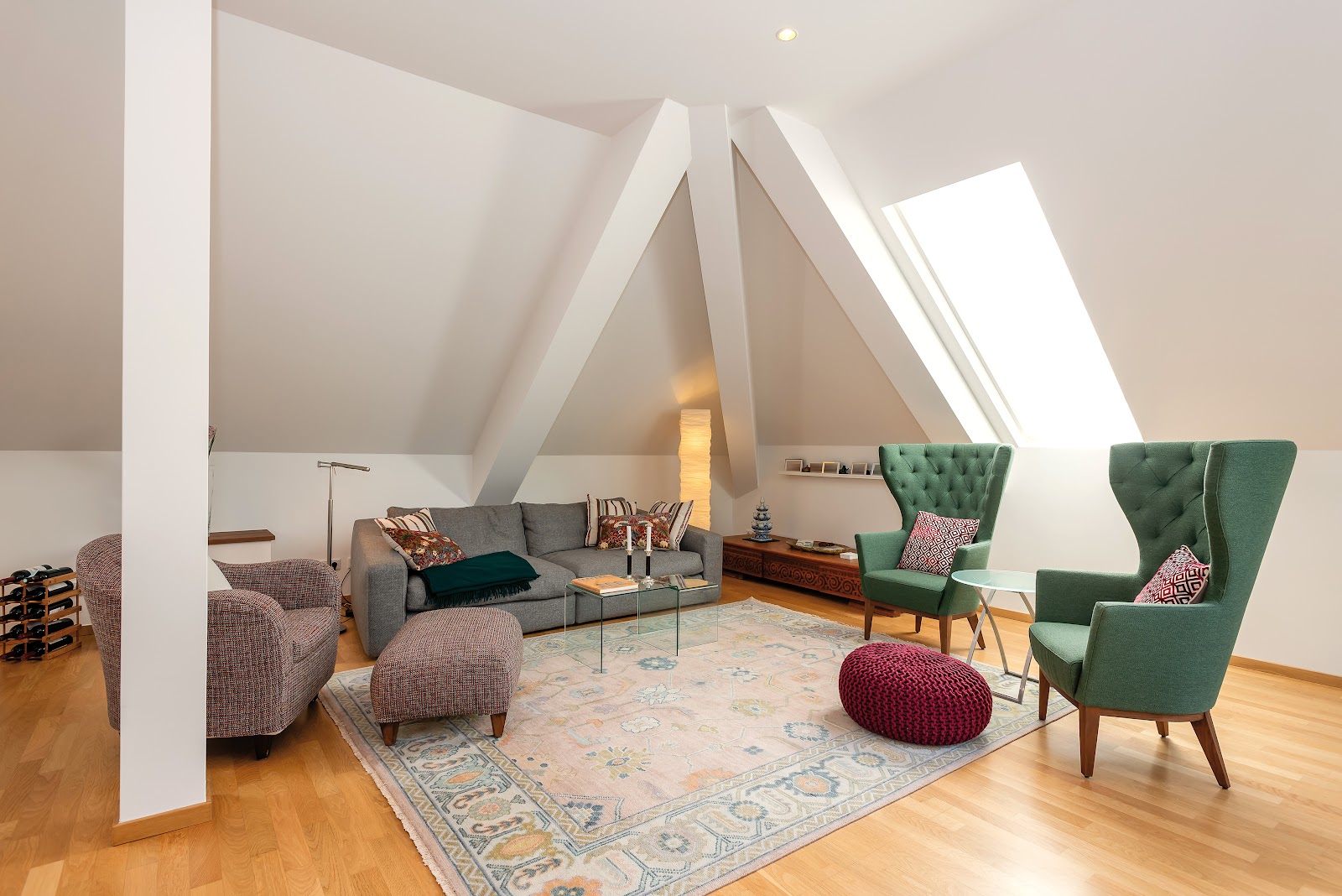 Ein renoviertes Wohnzimmer unter einer Dachschräge mit weißen Wänden, Holzboden und grünen Sesseln.