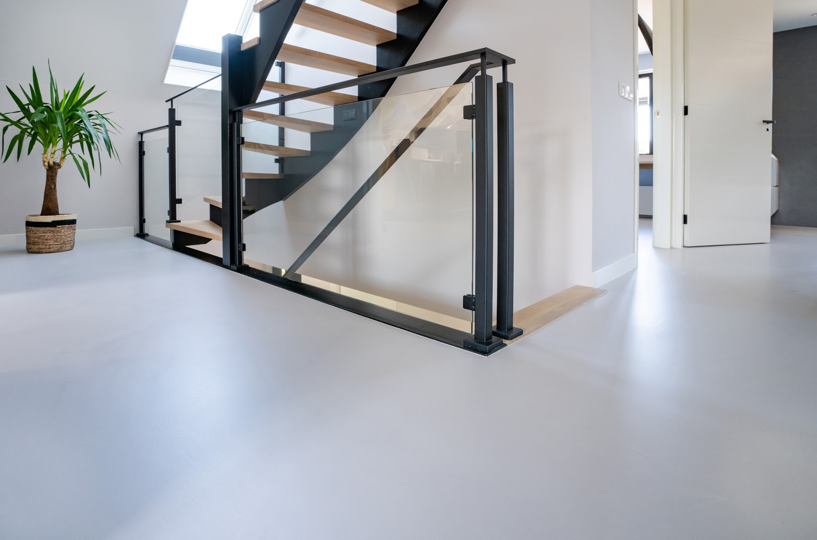 Moderne Treppe mit Holzstufen und schwarzem Geländer sowie ein glatter hellgrauer Boden in einem Wohnhaus.